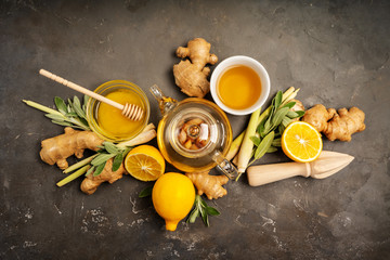 Making healthy antioxidant and anti-inflammatory ginger tea with fresh ginger, lemongrass, sage, honey and lemon on dark background with copy space. Top view.