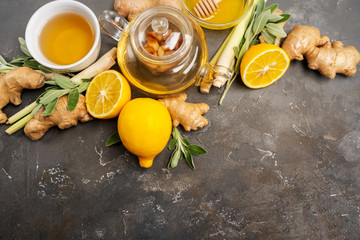 Making healthy antioxidant and anti-inflammatory ginger tea with fresh ginger, lemongrass, sage, honey and lemon on dark background with copy space.