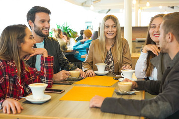 Group of people drinking cappuccino in a bar-  Friends hanging out with each other and talking- Smilie boys ang girls having conversations sitting around the coffee table- Lifestyle concept
