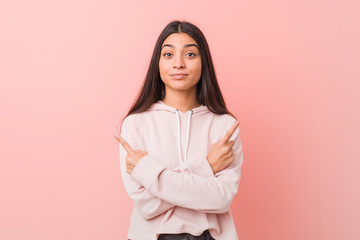 Young pretty arab woman wearing a casual sport look points sideways, is trying to choose between two options.