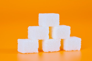 Pyramid from sugar cubes on a orange background. The pyramid is made up of sugar. Sugar cube