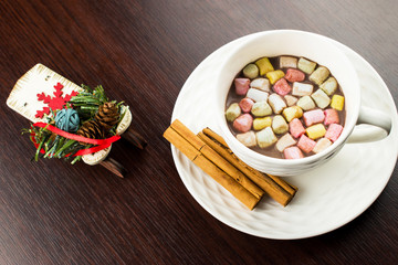 White cup on a white dish with hot chocolate and cinnamon sticks. Cinnamon sticks on a white saucer. A cup of hot shekolada before 