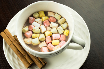 White cup on a white dish with hot chocolate and cinnamon sticks. Cinnamon sticks on a white saucer. A cup of hot shekolada before 
