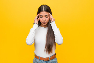 Young pretty arab woman against a yellow background touching temples and having headache.