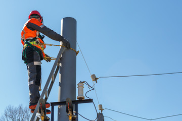 Working electrician tied to the pole with a safety rope