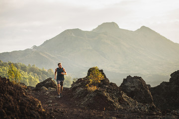 Young athlete man trail running in mountains in the morning. Amazing volcanic landscape of Bali...