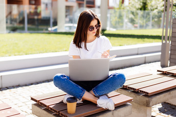Portrait of a beautiful young woman student studying on her laptop and writing notes in her...