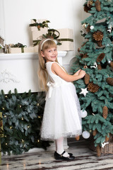 Cute little girl with long hair decorating christmas tree. Young kid in light bedroom with winter decoration. Happy family at home. Christmas New Year december time for celebration concept