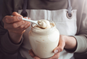 Mayonnaise in a glass jar and a spoon in a hand. Sour cream.