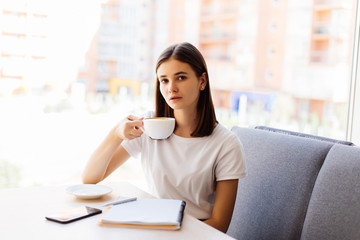 Modern girl sitting at the table drinking coffee and write notebook , A woman at cafe writing new story in notepad while drinking coffee
