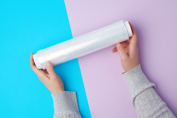 two hands hold a large roll of wound white transparent film for wrapping food