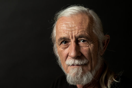 Closeup low key studio portrait of beautiful gray hair old man looking at the camera. Horizontally.