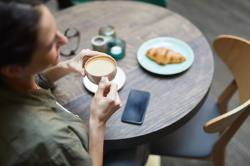 High angle view of smiling young woman holding cup of fresh coffee latte over wooden table in french cafe, copy space