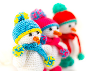 Three Little cute crocheted snowmans in a multicolor hats and scarfs on a white background.