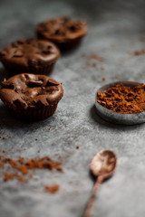 cocoa drink in blue mug with chocolate on dark textured background with chocolate muffins and vintage spoon and cocoa powder.