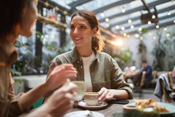 Portrait of beautiful young woman talking to friend while enjoying evening on outdoor terrace in cafe or coffee shop, copy space - obrazy, fototapety, plakaty