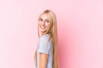 Young blonde woman on pink background looks aside smiling, cheerful and pleasant.