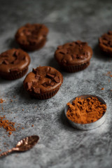 on a dark textured background with chocolate muffins and vintage spoon and cocoa powder.