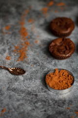 on a dark textured background with chocolate muffins and vintage spoon and cocoa powder.