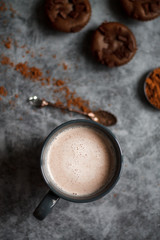 chocolate cocoa in blue mug on dark textured background with chocolate muffins and vintage spoon and cocoa powder.