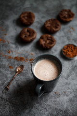 chocolate cocoa in blue mug on dark textured background with chocolate muffins and vintage spoon and cocoa powder.