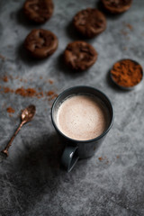 chocolate cocoa in blue mug on dark textured background with chocolate muffins and vintage spoon and cocoa powder.