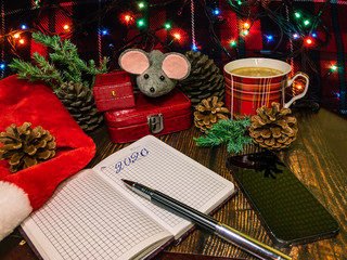 New Year mood. When you make plans for 2020. Notepad pen cup of coffee symbol of the year rat and smartphone on a wooden surface on a background of New Year's lights.