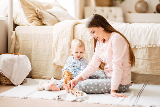 Young mother and son are playing in the bright room of his house. Cute baby boy with his mom. Happy and cute family chatting with baby
