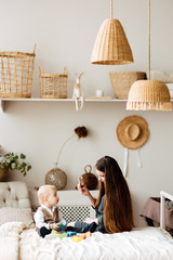 Young mother and son are playing in the bright room of his house. Cute baby boy with his mom. Happy and cute family chatting with baby