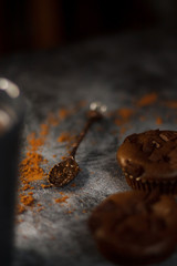 on a dark textured background with chocolate muffins and vintage spoon and cocoa powder.