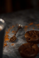 on a dark textured background with chocolate muffins and vintage spoon and cocoa powder.