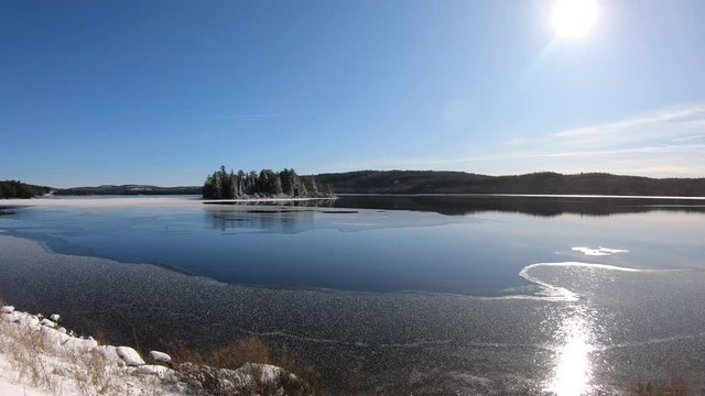 Algonquin Provincial Park with partly frozen iconic island in Lake of Two Rivers in a sunny winter day. Panning and hand held