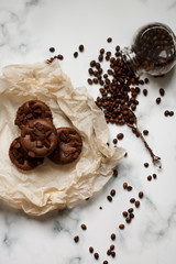 on a light textured marble background, chocolate muffins on parchment paper with a vintage spoon and coffee beans top view.