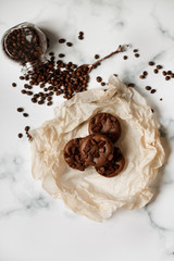 on a light textured marble background, chocolate muffins on parchment paper with a vintage spoon and coffee beans top view.