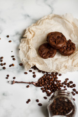 on a light textured marble background, chocolate muffins on parchment paper with a vintage spoon and coffee beans top view.