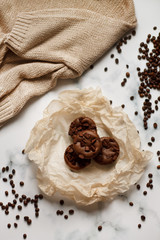 on a light textured marble background, chocolate muffins on parchment paper with a vintage spoon and coffee beans top view.