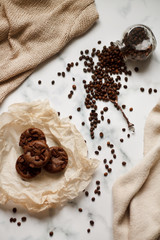 on a light textured marble background, chocolate muffins on parchment paper with a vintage spoon and coffee beans top view.