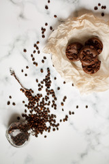 on a light textured marble background, chocolate muffins on parchment paper with a vintage spoon and coffee beans top view.