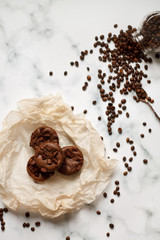 on a light textured marble background, chocolate muffins on parchment paper with a vintage spoon and coffee beans top view.