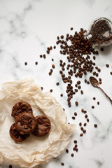 on a light textured marble background, chocolate muffins on parchment paper with a vintage spoon and coffee beans top view.