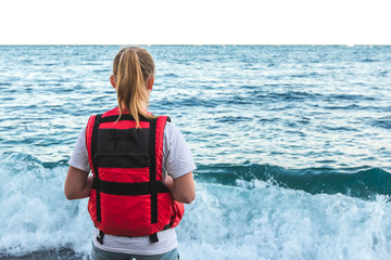 Blonde young girl in life jacket stands on the beach and watching waves. Lifeguard woman coast...