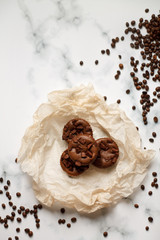 on a light textured marble background, chocolate muffins on parchment paper with a vintage spoon and coffee beans top view.