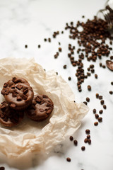 on a light textured marble background, chocolate muffins on parchment paper with a vintage spoon and coffee beans top view.