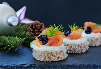 Party canapes with smoked salmon and caviar, closeup on black slate platter on the Christmas table, over dark background