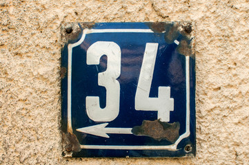 Weathered grunge square metal enameled plate of number of street address with number 34 closeup