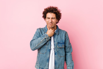 Fototapeta na wymiar Curly mature man wearing a denim jacket against pink background suffers pain in throat due a virus or infection.