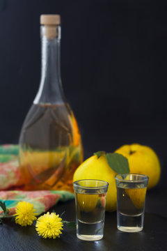 Quince brandy or quince vodka, hard liquor, strong drink in a bottle and glasses on dark background. Serebian traditional dring, rakija or rakia. Vertical image.