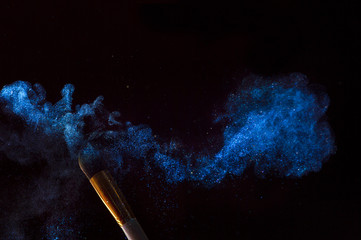 Make-up brush with blue powder explosion isolated on black background