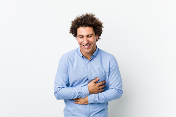 Young curly mature man wearing an elegant shirt laughs happily and has fun keeping hands on stomach.