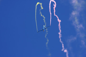 Glider performing aerobatics with smoke trails at airshow on sunny day in Switzerland